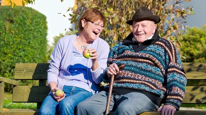 Senioren auf einer Bank bei Sonnenschein, Stock und Apfel in der Hand